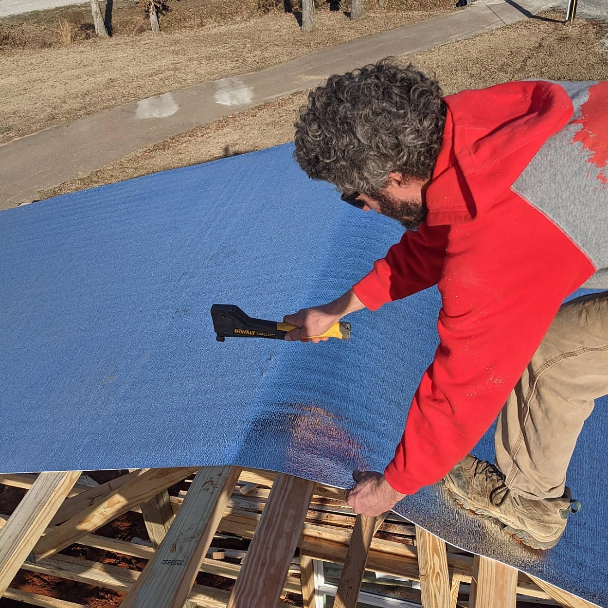Installer rolling ThermaGuard reflective insulation across roof framing