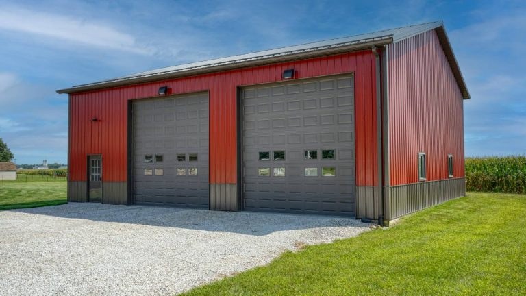Red post frame garage with two brown CHI overhead doors and a gravel drive